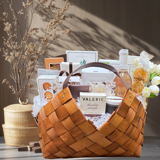 This is a photo of a large gift basket called grand epicurean. It is in a beautiful light brown woven gift basket with leather handles. It is packed full of delicious food items including gourmet chocolate bars, crackers, crisps, shortbread cookies, sparkling non- alcoholic beverage bottle, premium True Bloom Floral real Touch Flower Garnish, pitted olives, orange crisps, and more! Gift Basket, Gift, Luxury Gift, Luxury Gift Basket, Food Gift, Reno Gift, Biggest Little Baskets, Nevada Gift, Office Gift