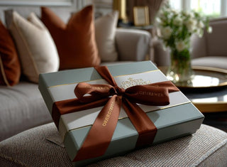 a green gift box sitting on an ottoman wrapped in a brown silk ribbon
