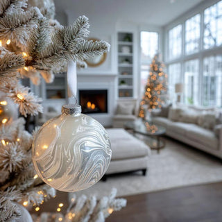 White marbled glass ornament with satin ribbon resting on snowy surface - artisan-blown 4.75 inch glass Christmas ornament for winter-white holiday styling.