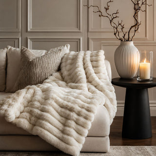 White textured throw blanket draped over a sofa in a living room setting with candles and decor.