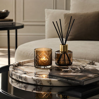 Decorative items on a marble tray including a candle and diffuser, with a couch and table in the background.