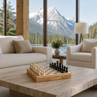 Burl wood chess and checker gift set styled on a stone coffee table in a mountain home living room with cream seating, warm wood accents, black and ivory chess pieces, and a scenic lake and mountain view. A strong gift choice for housewarming, real estate closing gifts, corporate clients, Father’s Day, holiday gifting, and anyone who enjoys classic games with a handsome home décor look.