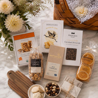 Flat-lay of the Classic Gourmet Charcuterie Gift Basket contents with an acacia board and representative seasonal sweet-and-savory selections.