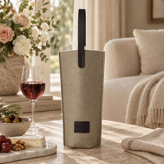 Clay Black Merino Wool Bottle Bag with leather handles displayed beside red wine, cheese, and olives on a stone table. The scene illustrates bottle-gifting presentation; only the bag is included.