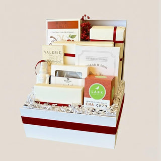 Open white Crimson & Cream holiday gift box with crimson ribbon, seasonal red berries, artisan cookies, chocolate, nuts, caramels, crackers, and ornament.