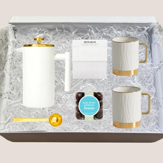 Open Deluxe Java Joy gift box with white-and-gold French press, two porcelain mugs, Monarch coffee, vanilla sugar cubes, espresso beans, and gold scoop.