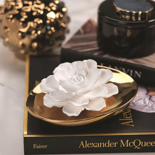 Close-up of the Dream white porcelain flower resting in its gold ceramic diffuser vessel, styled on fashion books with gold décor.