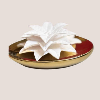 Close product view of the Dream white porcelain poinsettia flower resting in a low reflective gold ceramic fragrance vessel.