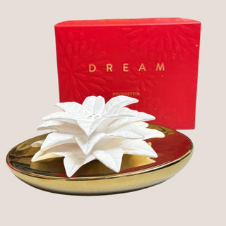 Dream porcelain poinsettia diffuser with a sculpted white holiday flower in a gold ceramic vessel displayed beside its red presentation box.