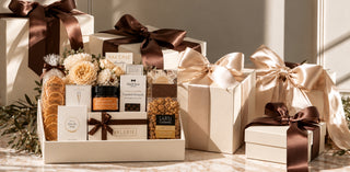 A luxury gift hamper set featuring a curated collection of gourmet items including artisanal breads, chocolates, and teas, beautifully arranged in a cream gift box with a dark brown ribbon, alongside matching cream gift boxes with satin ribbon bows.