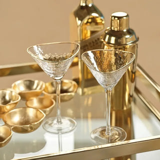 Pair of clear hammered martini glasses with gold rims styled beside a gold cocktail shaker on a mirrored bar tray.