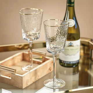 Pair of gold-rim hammered wine glasses styled beside a bottle of white wine on a warm metallic serving tray.