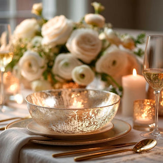 Gold and silver foiled glass bowl styled at a formal place setting with cream flowers, taper candles, votives, and a champagne flute.