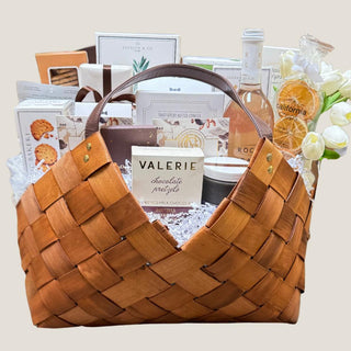 Front product view of the Grand Epicurean 21-inch woven gourmet gift basket filled with alcohol-free sparkling beverage, chocolates, crackers, crisps, cookies, spreads, and white faux botanicals.
