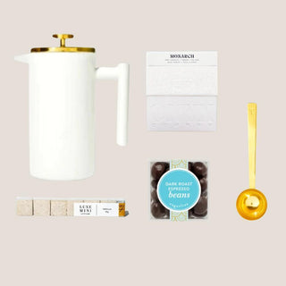 Java Joy contents arranged together with white-and-gold French press, whole-bean coffee, vanilla sugar cubes, dark-chocolate espresso beans, and brushed gold scoop.