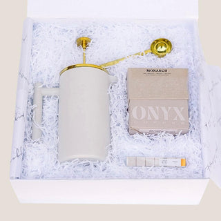 Open matte white Java Joy gift box with white protective fill holding the French press, coffee, vanilla sugar cubes, chocolate espresso beans, and gold scoop.