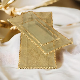Small Juliet clear glass tray stacked with coordinating rectangular gold scalloped trays beside white-and-gold tableware.