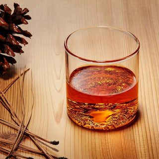 Luxury handcrafted Lake Tahoe Topographic Glass Tumbler with whiskey on a wood surface, styled with pinecone and pine needles, made in the USA and available from Biggest Little Baskets in Reno, Nevada, for nationwide luxury gifting and gift baskets.