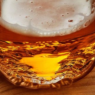 Extreme close-up of amber beer and foam inside a Lake Tahoe pint glass, showing the dimensional glass topography molded around the base.