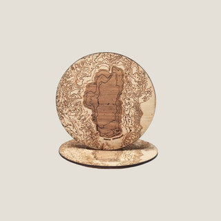Two round Lake Tahoe topographic wood coasters on a neutral background, with one upright to show the laser-etched lake and contour map.