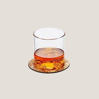 Clear lowball glass with amber whiskey resting on a round Lake Tahoe topographic wood coaster against a neutral background.