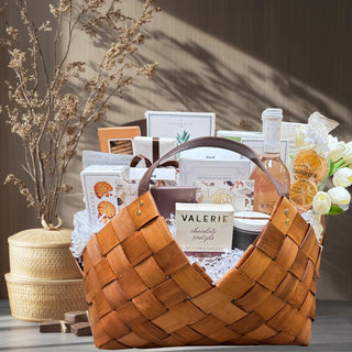 This is a photo of a large gift basket called grand epicurean. It is in a beautiful light brown woven gift basket with leather handles. It is packed full of delicious food items including gourmet chocolate bars, crackers, crisps, shortbread cookies, sparkling non- alcoholic beverage bottle, premium True Bloom Floral real Touch Flower Garnish, pitted olives, orange crisps, and more! Gift Basket, Gift, Luxury Gift, Luxury Gift Basket, Food Gift, Reno Gift, Biggest Little Baskets, Nevada Gift, Office Gift