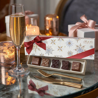 Limited edition Ethel M chocolate caramels in red ribbon holiday box photographed on luxury marble table with champagne and candles for Biggest Little Baskets