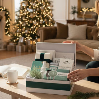 Woman holding the Minted Moment holiday gift box filled with artisan treats, chocolates, and a white nutcracker ornament, styled with faux cedar and velvet ribbon in a softly lit modern home with festive holiday décor.