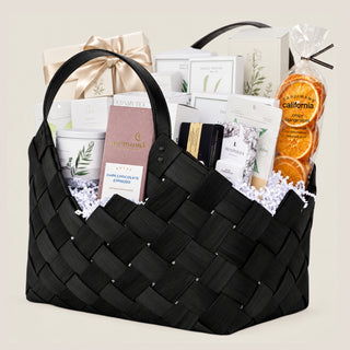 Angled product view of the black 21-inch Office Harmony woven basket with leather-style handles and a layered seasonal gourmet assortment.