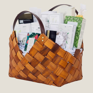 Angled product view of the brown 21-inch Office Harmony woven basket with leather-style handles and a layered seasonal gourmet assortment.