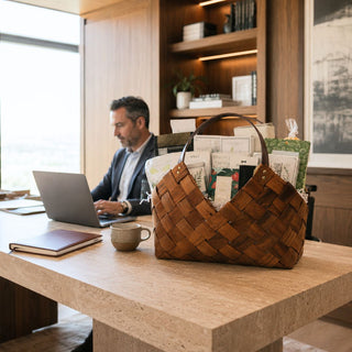 Professional seated at a modern office desk beside a large brown Office Harmony gourmet gift basket with seasonal sweet and savory foods.