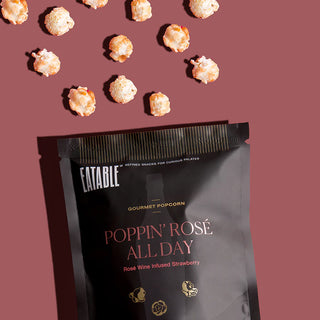 Edible 'Poppin' Rosé All Day' gourmet popcorn packaging with scattered popcorn on a pink background.
