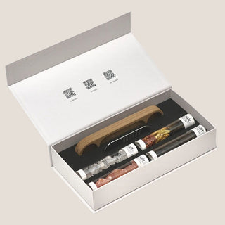 Open Rivsalt gift box with a metal grater, wooden stand, and four seasoning tubes arranged in a black insert.