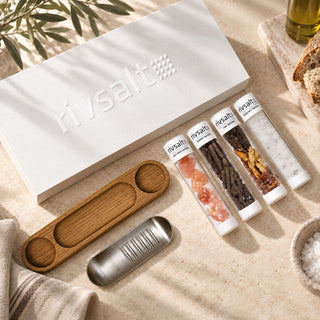 Rivsalt seasoning gift set on stone with a white box, metal grater, wooden stand, and four seasoning tubes.