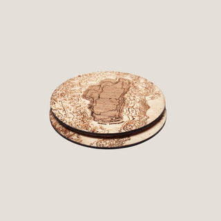 Set of two round Lake Tahoe topographic birch coasters stacked at an angle, showing the etched lake map and dark cork-backed edges.