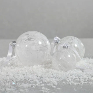 Set of white marbled glass ornaments with satin ribbons sewing on snowy surface - elegant handcrafted holiday ornaments for neutral Christmas styling.