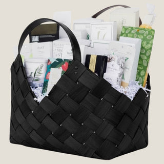 “Side view of modern black woven gift basket overflowing with wellness and gourmet products on neutral backdrop – curated luxury gift basket for corporate appreciation, hospitality, or home gifting.”