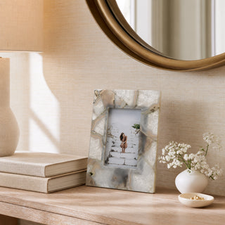 A rectangular photo frame with a textured, metallic silver and white marbled pattern stands on a wooden console table. The frame contains a sample photo of a woman on a beach.