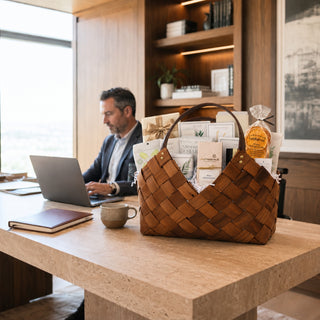 Professional seated at a modern office desk beside a large brown Office Harmony gourmet gift basket with seasonal sweet and savory foods.