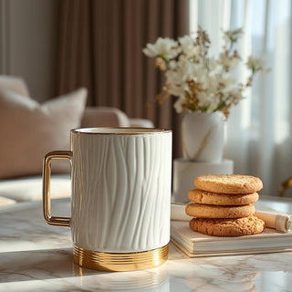 White mug with gold accents on a marble surface with cookies and flowers in the background