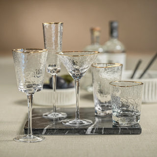 Two hammered glass wine glasses with gold rims on a gray marble tray beside a bottle of white wine – elegant bar cart setup.Third & Main