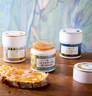 Jars of confiture with a spoon on a wooden surface, with a colorful abstract painting in the background.