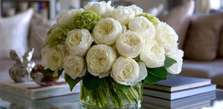 Bouquet of white and green flowers, austin roses, artificial florals in a glass vase on a table with a blurred background