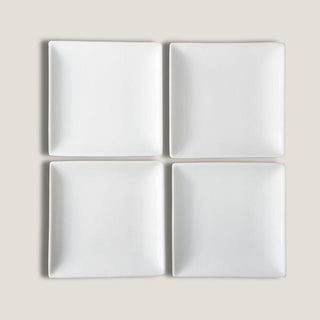 Set of four small white square porcelain plates arranged together against a warm neutral background.
