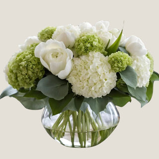 Full green and white hydrangea, rose and Austen rose arrangement in a rounded clear glass vase with visible stems.