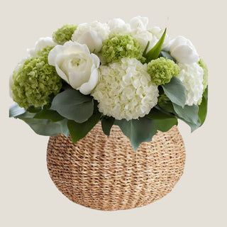Green and white real-touch hydrangea and rose arrangement in a rounded woven seagrass vase.