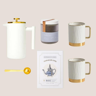 Flat lay of the Luxe Tea Indulgence Gift Box with French press, two white-and-gold mugs, Charles Grey tea, shortbread, and gold scoop.