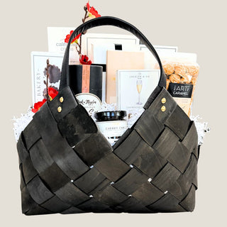 Front view of The Marlowe medium black woven basket filled with cookies, chocolate, popcorn, citrus, crackers, and seasonal botanicals.