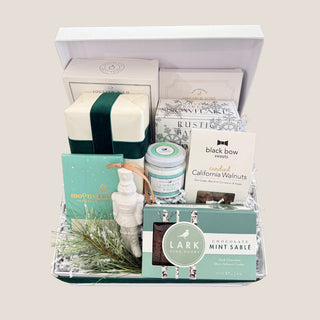 Open Minted Moments gift box with artisan treats, white ceramic nutcracker ornament, faux cedar, and green velvet ribbon.