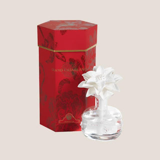 White porcelain poinsettia fragrance diffuser in a clear glass bottle beside its tall red holiday presentation box.